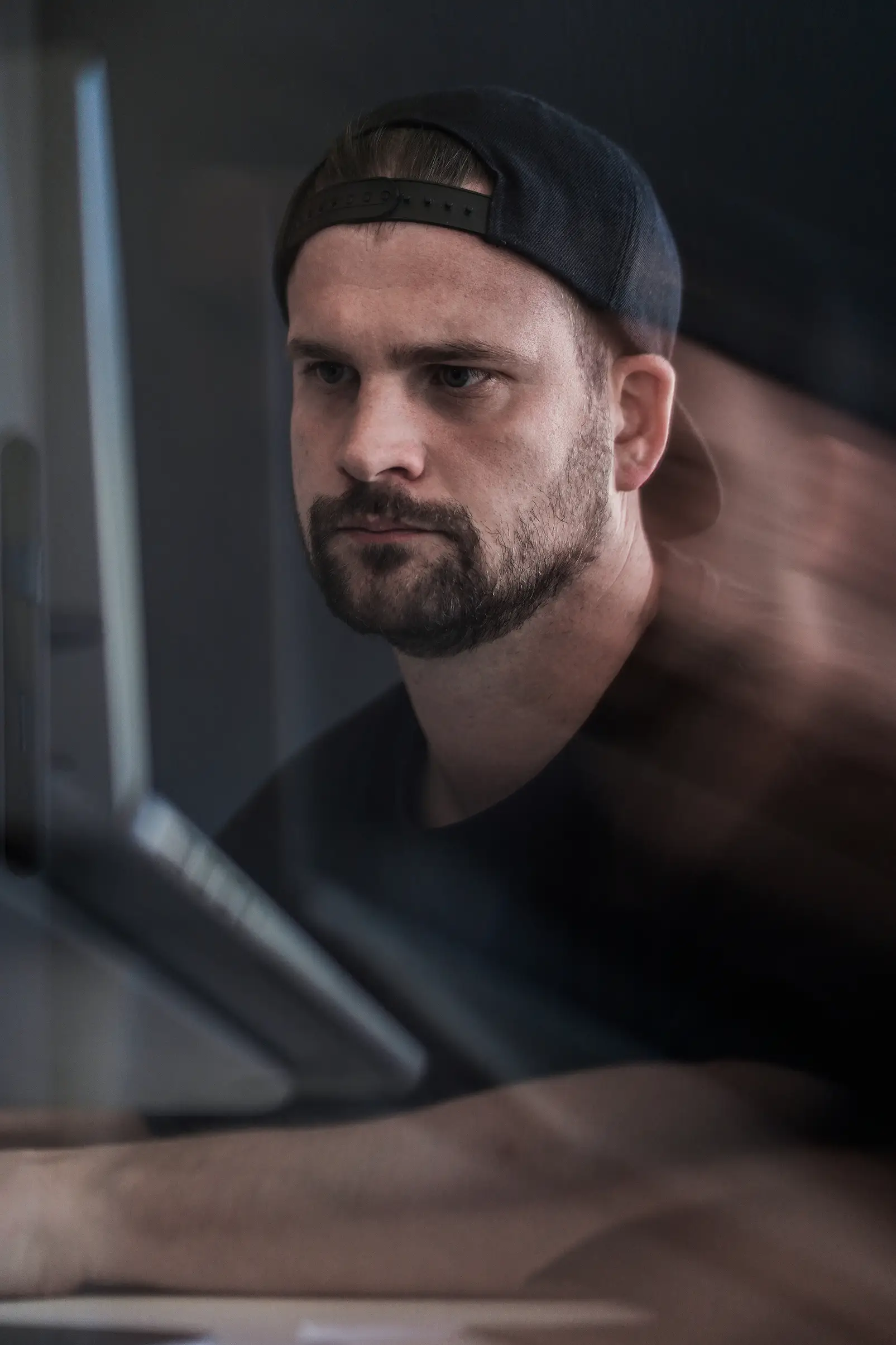 Mann mit Cap und Bart blickt konzentriert auf einen Bildschirm, im Vordergrund verschwommene Reflexionen.